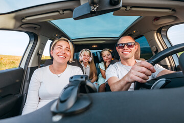 A happy young couple with two daughters inside the car during auto trop. They are smiling, and laughing during a road trip. Family values, traveling concepts.