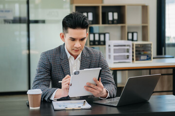 Confident Asian man with a smile standing holding notepad and tablet at the modern office.