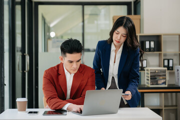Asian business colleague business presents and explains and using laptop and tablet. Teamwork, financial marketing team,   while sitting in modern office