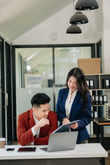 Asian business colleague business presents and explains and using laptop and tablet. Teamwork, financial marketing team,   while sitting in modern office