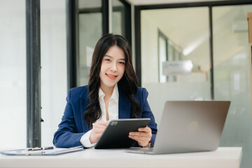 Confident business expert attractive smiling young woman typing laptop ang holding digital tablet on desk in creative office.