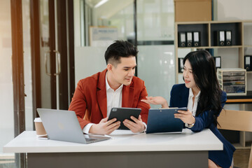 Asian business colleague business presents and explains and using laptop and tablet. Teamwork, financial marketing team,   while sitting in modern office