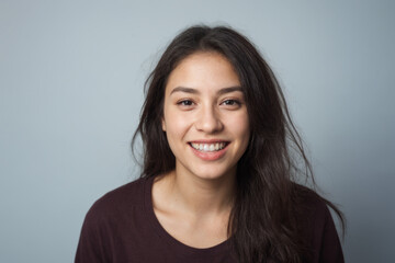 Everyday people. A smiling woman with long brown straight hair over her shoulder. Wearing a brown tshirt. Pretty woman. University student. On a light grey studio background. Portrait.
