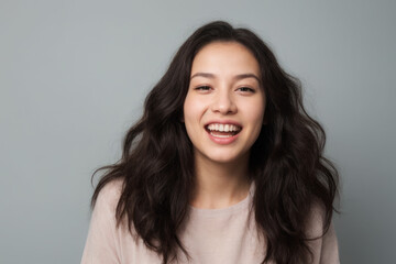 Everyday people. A happy asian woman laughing. Black wavy hair to her shoulders. Wearing a white shirt. Pretty woman. University student. On a light grey studio background. Portrait.