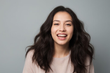 Naklejka premium Everyday people. A happy asian woman laughing. Black wavy hair to her shoulders. Wearing a white shirt. Pretty woman. University student. On a light grey studio background. Portrait.