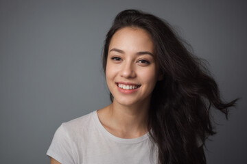 Everyday people. A happy asian woman laughing. Black windswept wavy hair to her shoulders. Wearing a white shirt. Pretty woman. University student. Wholesome. On a grey studio background. Portrait.