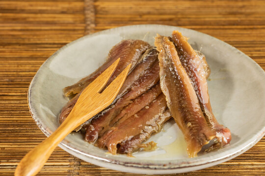 Poisson marin&eacute; dans de l'huile d'olive, filets de hareng dans une assiette &eacute;maill&eacute;e avec un pique en bois &agrave; 2 dents, sur un fond en rotin