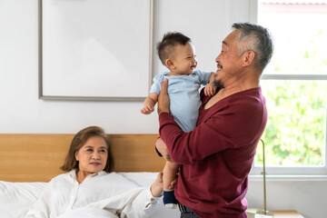 Portrait of happy love asian grandfather with grandmother playing with asian baby on bed, senior,...