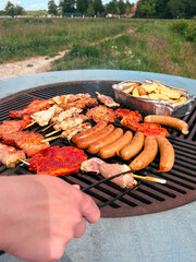 People grilling meat and sausage on a grill outside. Grilling pork fillet on charcoal grill. Vertical photo. Picnic outside barbecue in summer day.