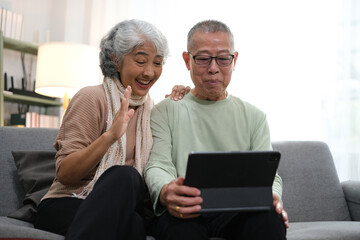Obraz premium senior couple sitting on sofa using tablet while video call online with family in living room at home