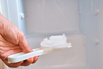 A man holds a shovel with ice on the background of a freezer. Defrosting the freezer.