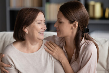 Naklejka premium Close up beautiful adult daughter hugs lovely aged mother loving women different generations relatives females sit on couch looking at each other feels happy spend time together, love and care concept