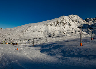  Paisagem de montanhas ao fundo e neve branca no chão e céu azul.