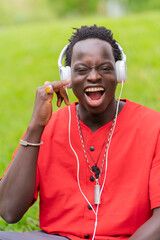 Happy young black man listening to music with headphones in park.