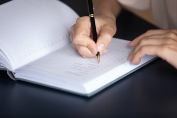 Housewife holding pen creates household to-do list using personal organizer seated at table, close up view. Businesswoman writing on diary, keeps daily record of events, appointment. Wish list concept