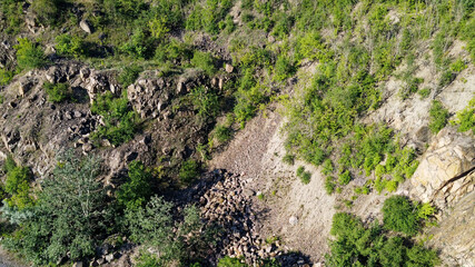 The rocky slopes of the hill are overgrown with bushes and small trees. Rocky terrain, aerial view.