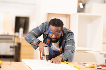 African American man does his work at furniture factory seriously and professtionally, carpenter ocupation, labor job holliday., using machine for work