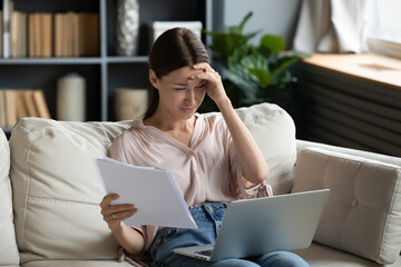 Stressed woman holds papers looking at laptop screen check online e-banking statement feels desperate, financial pressure and problems, not enough money, late bill payments and increasing debt concept