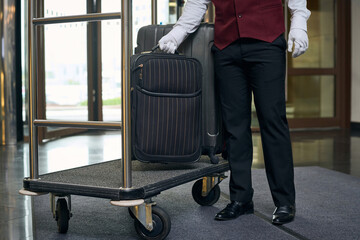 Close-up of doorman in uniform putting luggage on trolley in the lobby of the hotel