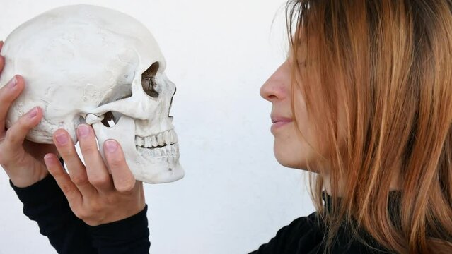 Close-up of a pretty young woman kissing a human skull on the teeth