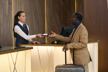Receptionist giving key from room to guest during his check-in in the hotel