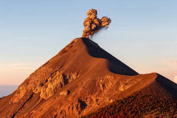 Volcan or volcano Fuego erupting with orange smoke column at sunrise, clear day near Antigua, Guatemala, Central America
