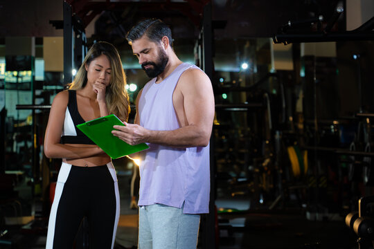 young woman consult in body analysis progress and planning diet with personal trainer at modern gym, active fitness people workout weight training strength body and mental health in dark sport club