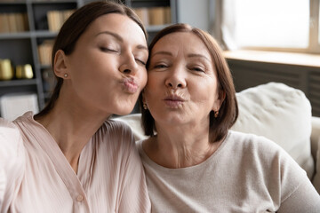 Vlogger women using smartphone recording new video vlog, faces of middle-aged mother and grown up adult daughter looking at camera blowing kisses pouting lips making selfie photo, webcam close up view