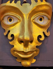 A golden mask with big eyes, long nose, thin lips and cheeks and forehead in curvy designs,
