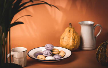 A plate with pumpkin-flavored macaroons. Cooked homemade cookies with rustic recipe. Pastry based on meringue from almond flour. Orange pumpkin in a background. Thanksgiving day table. Vintage photo