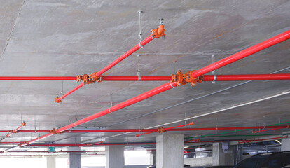 Red fire protection water pipeline system with sprinkler on concrete ceiling inside of parking garage building, perspective side view - obrazy, fototapety, plakaty