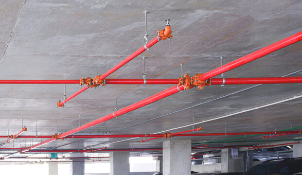 Red fire protection water pipeline system with sprinkler on concrete ceiling inside of parking garage building, perspective side view