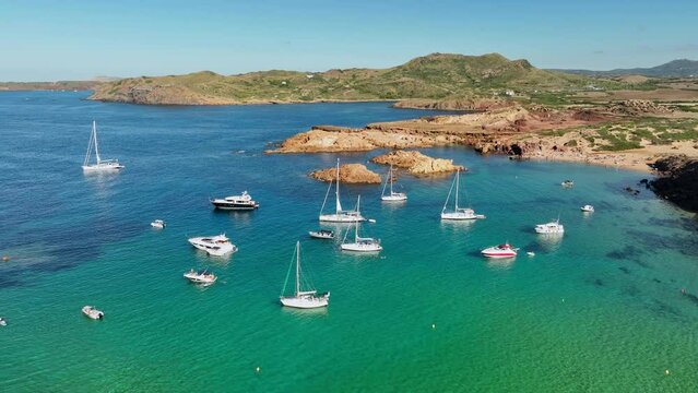 A serene view of sailboats anchored at Cala Pregonda in Minorca, set against the backdrop of rugged coastlines.