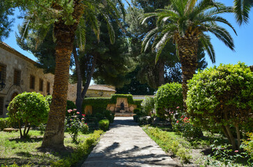 View of a rest plaza with palm trees and vegetation with a stone and cement hallway and a statue at the end of it