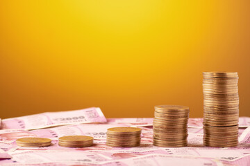Indian currency coin stack with rupee note on yellow background