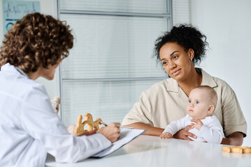 Young mother with child listening to doctor while sitting at table in her office