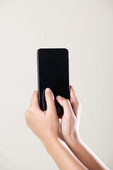 Both hand hold black screen smartphone vertically on grey background