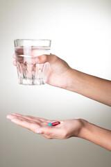 Medicine and glass of water in hand on grey background