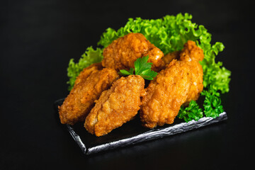 Chicken wings fried until half cooked, semi-finished product.Semi-finished chicken wings on a dark background with fresh herbs. Half-finished. Quick cooking at home. Fast food. Breaded chicken wings.