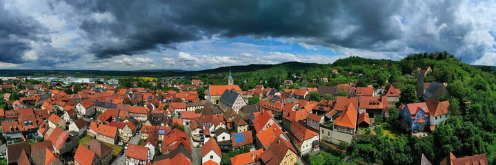 Luftbild von Königsberg in Bayern. Die Stadt ist von Hügeln und Wäldern umgeben. Der Himmel ist bewölkt und dunkel und deutet auf einen herannahenden Sturm hin. 