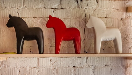 Black, red and white purchased figurines of horses against a white brick wall on a wooden shelf