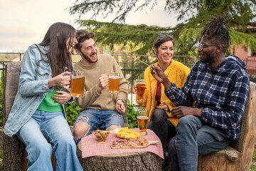 Outdoor Gathering with Friends - Friends laughing and drinking beers outdoors around a tree trunk table with snacks. Garden setting, relaxed atmosphere. - obrazy, fototapety, plakaty