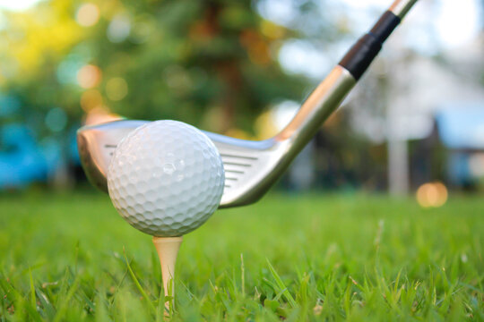 A golf ball is set on a tee in the grass and is hit with the head of a golf club.