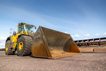 Heavy duty yellow tractor on the road near belt conveyor. Front End Loader
