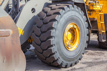 Close up view of the big yellow tractor. Wheel tire of the front end loader