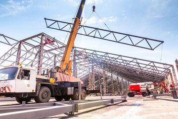 Installation of metal rafter trusses of the covered warehouse with a car crane. Metall frame storage building