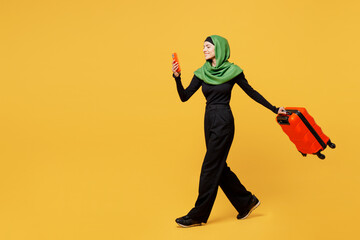 Fototapeta na wymiar Traveler arabian asian muslim woman wear green clothes hold bag mobile cell phone isolated on plain yellow background. Tourist travel abroad in free time rest getaway. Air flight trip journey concept.