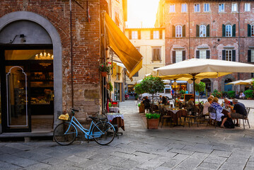 Old cozy street with tables of restaurant in Lucca, Italy - obrazy, fototapety, plakaty