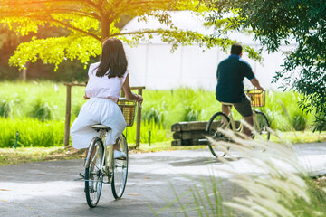 Young Happy Asian woman rides bicycle in sunny park. Woman ride bicycle with having fun to exercise activity with healthy lifestyle in garden. Chilling and relaxing young Asian woman enjoys nature.