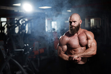 Fototapeta na wymiar Muscular bald man posing shirtless. Bodybuilder showing off his shape in the gym. 
